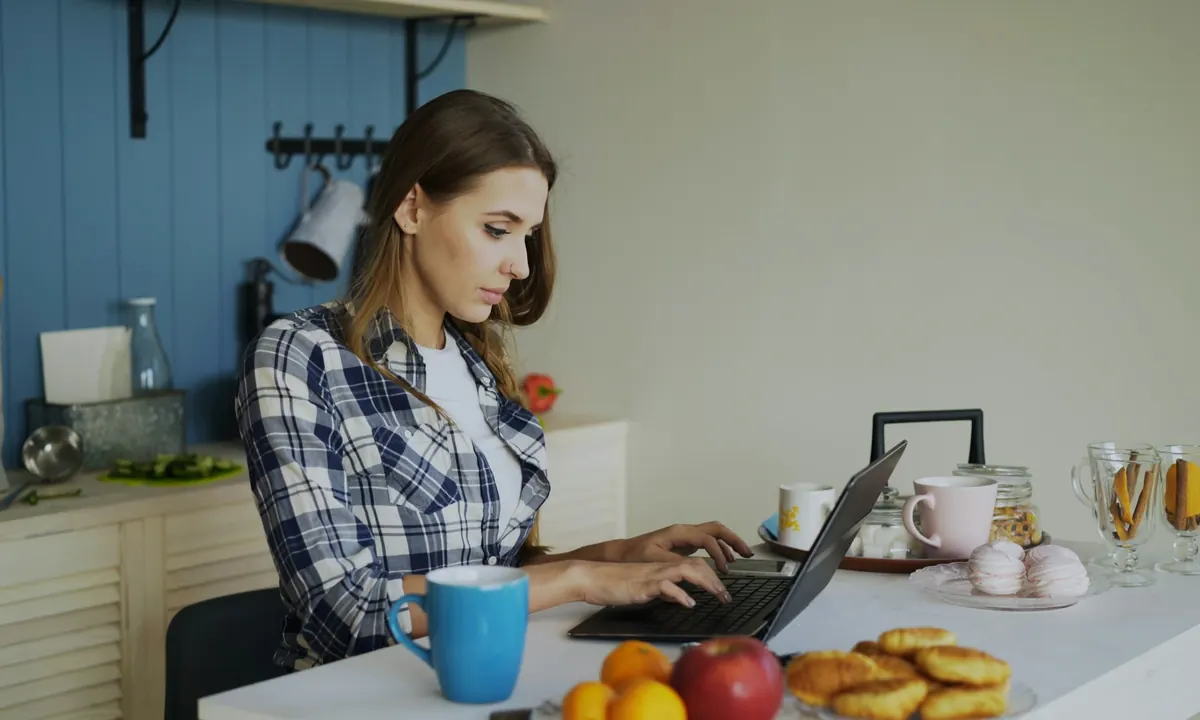 A woman working on a laptop at a kitchen table