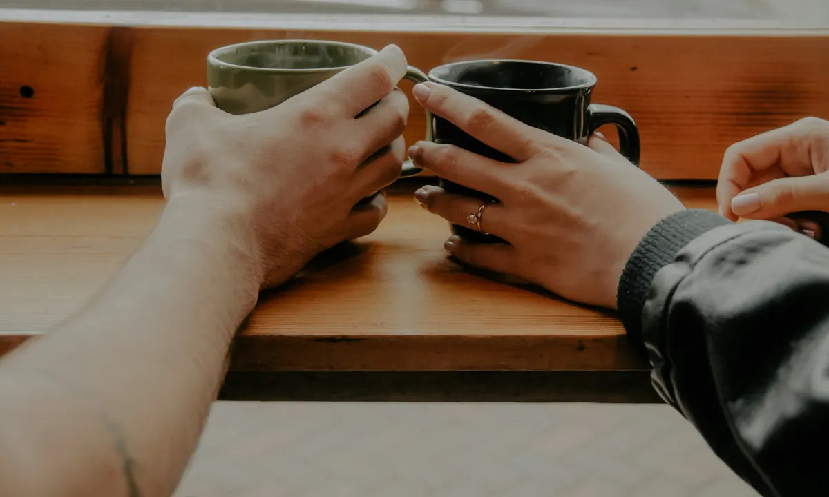 Two people holding mugs of coffee across a table