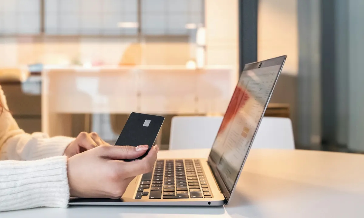 A woman holding a bank card in front of a laptop