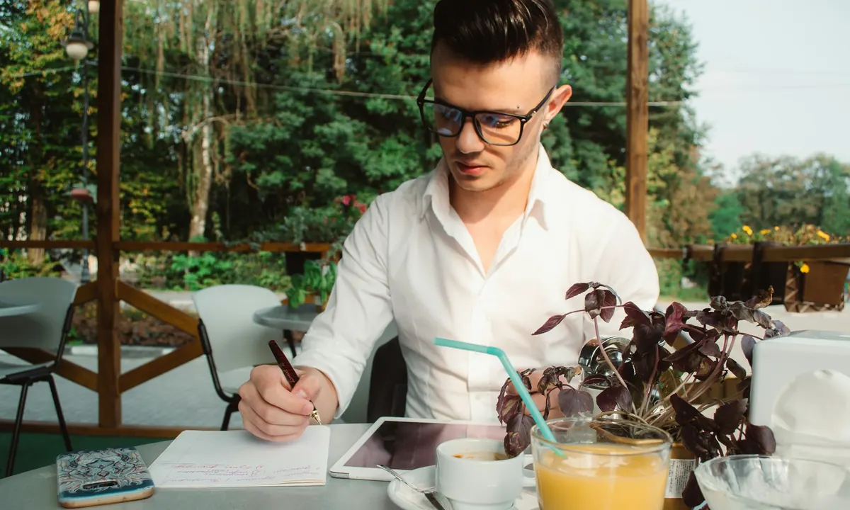 A man writing notes at an outdoor cafe table